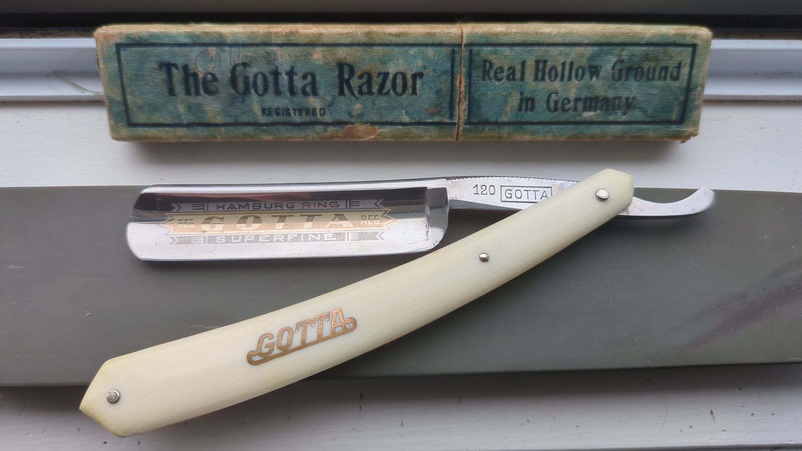 Gotta 120 6/8 straight razor open, with cream celluloid scales marked Gotta in gold and the gilded Hamburg Ring etch, in front of its original box printed The Gotta Razor, Real Hollow Ground in Germany