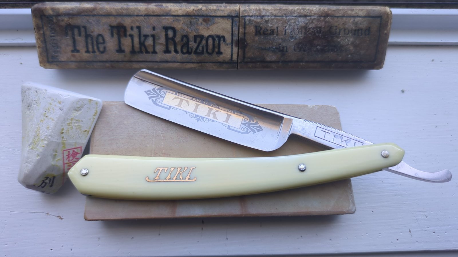 Tiki straight razor with cream celluloid scales marked Tiki in gold, the blade etched TIKI, in front of its original box